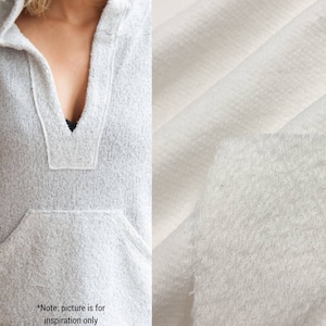 May include: A white hooded sweatshirt with a v-neck and a pocket. The fabric is a soft, textured knit.