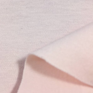 May include: Close-up of a soft, white fabric with a subtle texture. The fabric is folded over, revealing a lighter shade of pink underneath.