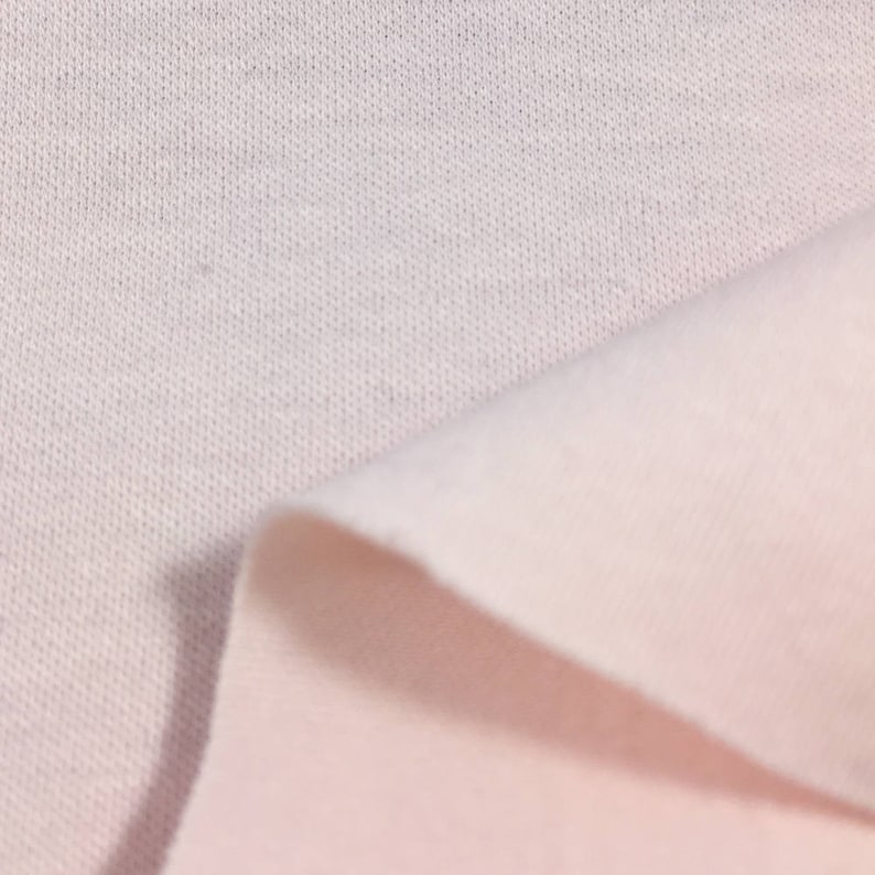 May include: Close-up of a soft, white fabric with a subtle texture. The fabric is folded over, revealing a lighter shade of pink underneath.