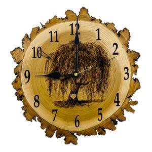 May include: A wooden clock with a black face and black hands. The clock is shaped like a tree trunk and has a burned-in image of a weeping willow tree. The numbers on the clock face are black and the clock has a heart in the center.