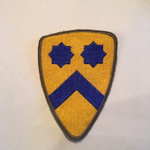 May include: A yellow military patch with a blue chevron and two blue eight-pointed stars.