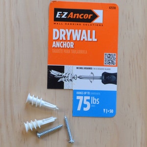 Puede incluir: Un primer plano de un paquete de anclaje para paneles de yeso con un anclaje de pl&aacute;stico blanco y un tornillo. El paquete es naranja y azul y dice "E-Z Ancor" y "Drywall Anchor". El anclaje est&aacute; clasificado para 75 libras.