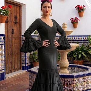 May include: A floor-length black dress featuring a V-neckline, long sleeves with tiered ruffled cuffs, and a multi-tiered ruffled hem. The garment is accessorized with large gold hoop earrings and a vibrant purple floral hair accessory.