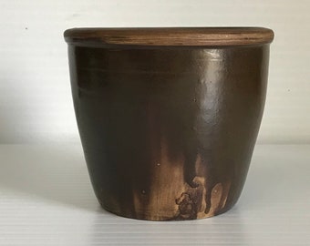 May include: A dark brown ceramic planter with a wooden rim. The planter has a slightly rounded shape and a smooth, glossy finish.