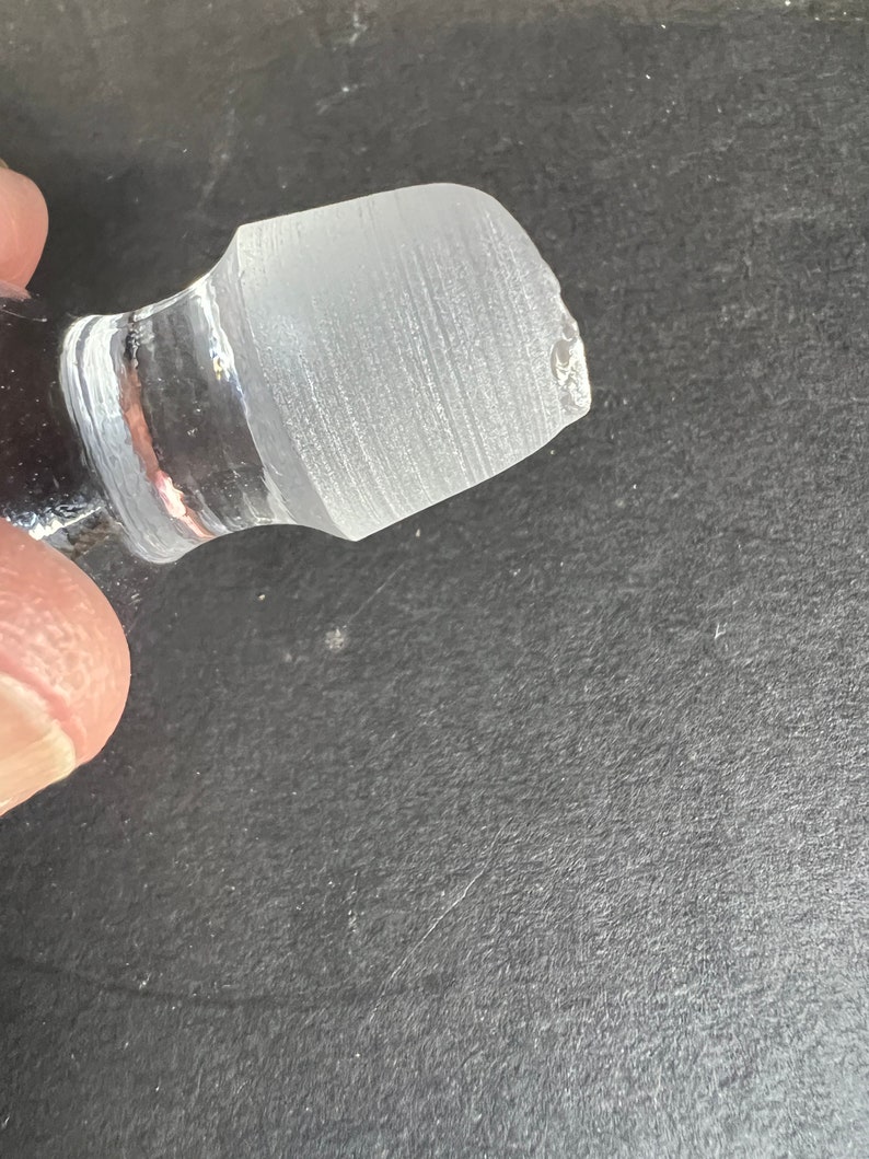 May include: Clear glass bottle stopper with a frosted top. The stopper has a slightly chipped edge.