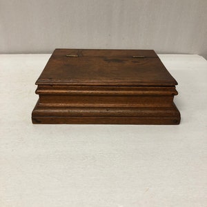 May include: A dark brown wooden box with a hinged lid and brass hinges. The box has a simple, rectangular shape and a smooth, polished finish.
