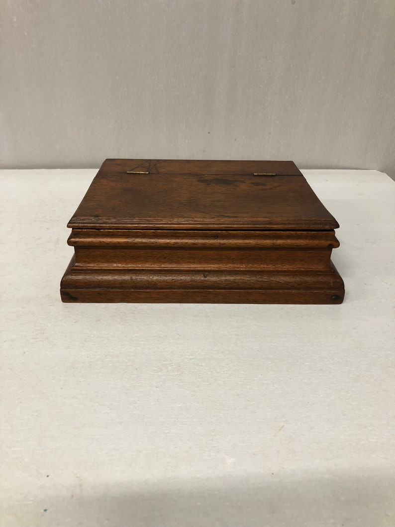 May include: A dark brown wooden box with a hinged lid and brass hinges. The box has a simple, rectangular shape and a smooth, polished finish.