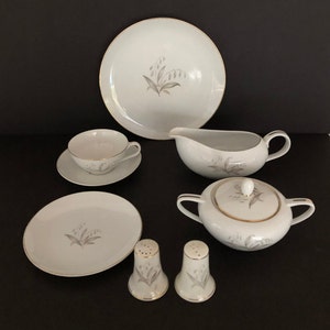 May include: A set of white porcelain dinnerware with a delicate gray floral design and gold trim. The set includes a large platter, a gravy boat, a sugar bowl with lid, two salt and pepper shakers, a teacup and saucer, and a small plate.