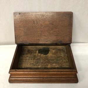 May include: A wooden box with a hinged lid. The inside of the box is lined with wood. The lid has the initials "AK" written on it.