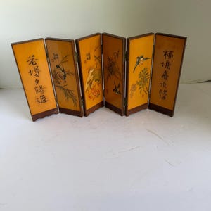 May include: A six-panel folding screen featuring a warm yellow finish with dark brown wooden frames. Each panel displays detailed illustrations of birds, bamboo, and floral elements, accompanied by black Chinese calligraphy characters.