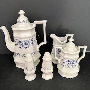 May include: A white porcelain tea set with blue floral designs. The set includes a teapot, creamer, sugar bowl, and two salt and pepper shakers.