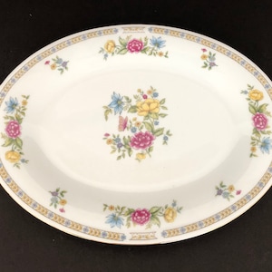 May include: White oval serving platter with a gold rim and floral design. The floral design features pink, yellow, and blue flowers with green leaves. There is a butterfly in the center of the design.