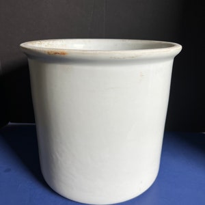 May include: White ceramic utensil holder with a slightly rounded top and a smooth, white finish.