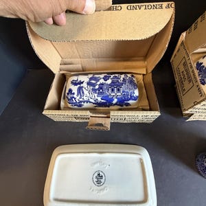 Peut inclure: Beurrier en c&eacute;ramique bleu et blanc avec un motif de paysage, pr&eacute;sent&eacute; dans une bo&icirc;te en carton. Le plat rectangulaire a un couvercle, et la bo&icirc;te est &eacute;tiquet&eacute;e "Churchill of England". Un deuxi&egrave;me plat est visible.