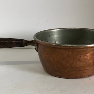 May include: A small copper saucepan with a wooden handle. The saucepan has a silver lining.