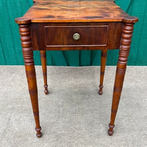 May include: A small, wooden table with a single drawer and turned legs. The table has a dark brown finish and a simple design.