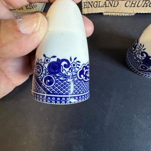 Peut inclure: Salerette en c&eacute;ramique blanche avec un motif floral et g&eacute;om&eacute;trique bleu autour de la base. La salerette a un dessus arrondi. Le design rappelle la porcelaine classique bleue et blanche. La salerette est tenue par une main.