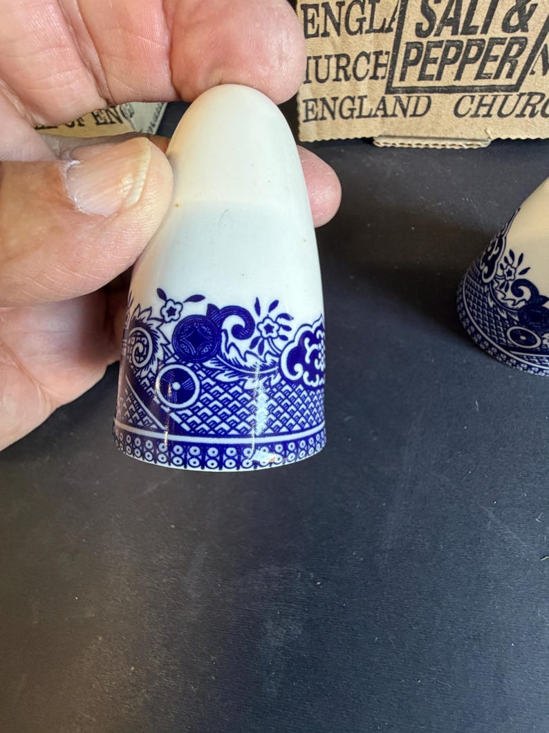 Peut inclure: Salerette en c&eacute;ramique blanche avec un motif floral et g&eacute;om&eacute;trique bleu autour de la base. La salerette a un dessus arrondi. Le design rappelle la porcelaine classique bleue et blanche. La salerette est tenue par une main.