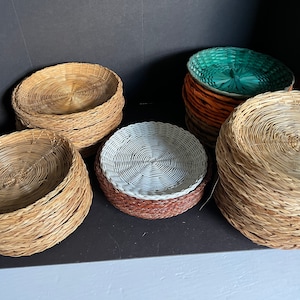 May include: A set of woven wicker plates in various colors, including natural, white, and green. The plates are stacked in piles and are perfect for adding a rustic touch to any table setting.