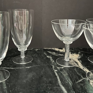 May include: Set of eight clear glass drinking glasses with a twisted stem design. The glasses are arranged in two rows, with four glasses in each row.