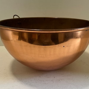 May include: A large, copper mixing bowl with a single handle. The bowl is shiny and has a slight patina.
