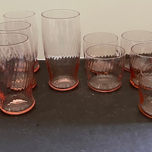 May include: Set of 12 pink glass tumblers with a textured design. The tumblers are in two sizes, with the larger ones being taller and narrower. The tumblers are all clear glass with a pink tint.