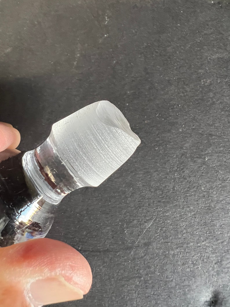May include: Close-up of a clear glass bottle stopper with a textured surface.