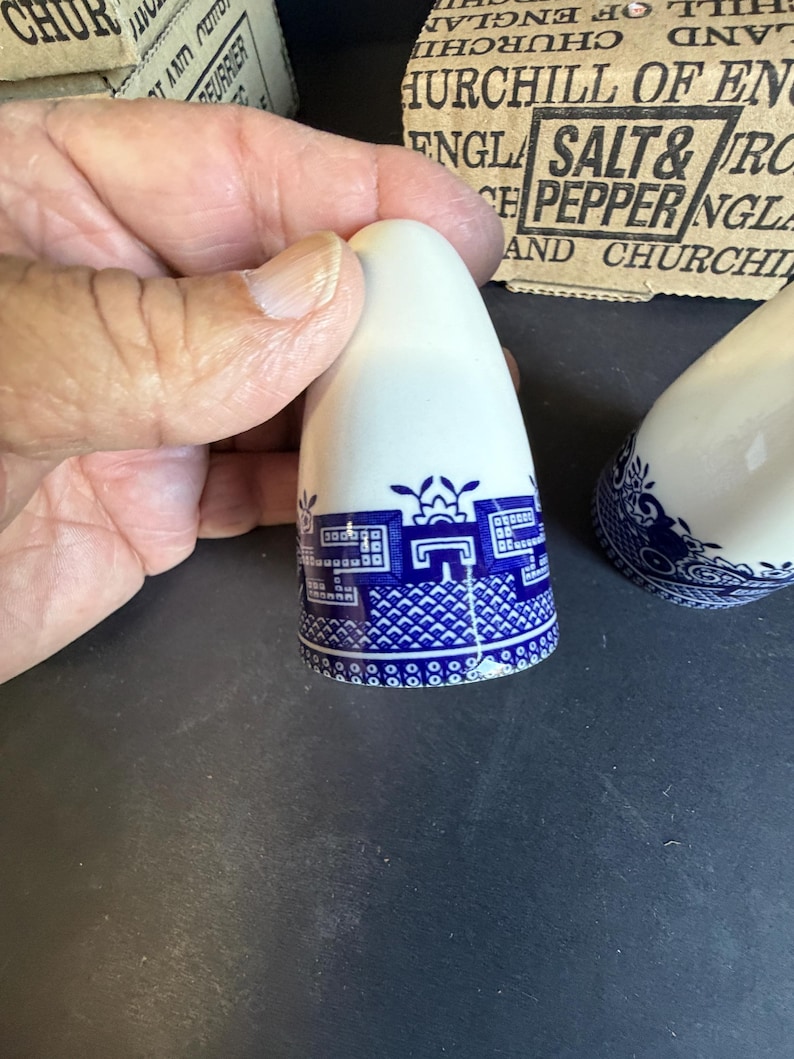Peut inclure: Sali&egrave;re et poivri&egrave;re en c&eacute;ramique blanche avec un motif d&eacute;coratif bleu et blanc. Les sali&egrave;res et poivri&egrave;res ont un dessus arrondi et un motif d&eacute;taill&eacute; autour de la base. L'emballage en arri&egrave;re-plan indique "Churchill of England Salt & Pepper".