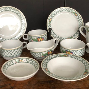 May include: A set of white ceramic dishes with a green and yellow floral pattern. The set includes a large plate, a small plate, a bowl, a mug, a creamer, and a sugar bowl.
