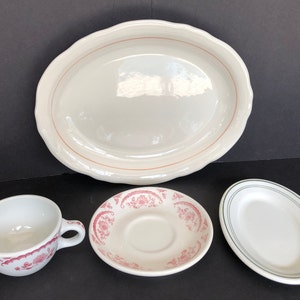 May include: A set of four white ceramic plates with pink and green floral designs. The set includes a large oval platter, a smaller oval plate, a saucer, and a teacup.