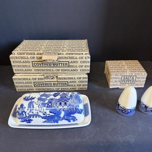 Peut inclure: Un plat &agrave; beurre couvert bleu et blanc avec un motif de paysage, deux sali&egrave;res et poivri&egrave;res, et des bo&icirc;tes avec l'inscription "Covered Butter" et "Salt & Pepper". Les articles sont en c&eacute;ramique.