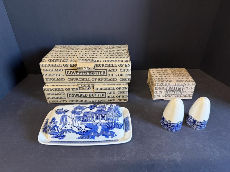 Peut inclure: Un plat &agrave; beurre couvert bleu et blanc avec un motif de paysage, deux sali&egrave;res et poivri&egrave;res, et des bo&icirc;tes avec l'inscription "Covered Butter" et "Salt & Pepper". Les articles sont en c&eacute;ramique.