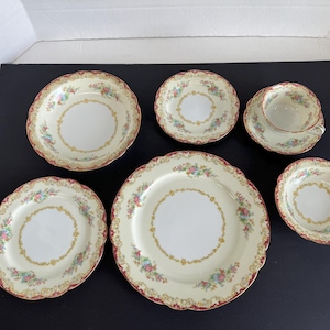 May include: A set of vintage Japanese porcelain dinnerware with a floral pattern in shades of pink, blue, and green. The set includes a large dinner plate, a salad plate, a soup bowl, a bread and butter plate, a teacup, and a saucer.