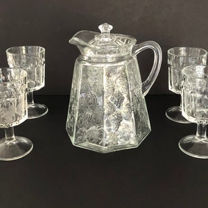 May include: A set of four clear glass wine glasses with a pitcher. The glasses and pitcher have a textured, etched design.