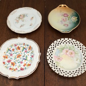 May include: Four decorative antique plates with floral designs. One plate has a gold rim and a floral pattern. Another has a scalloped edge and a floral design. The third plate has a lattice edge and a floral design. The fourth plate has a gold rim and a floral pattern.