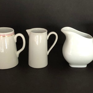 May include: Five white ceramic creamer pitchers with different floral designs. The pitchers are all different sizes and shapes.