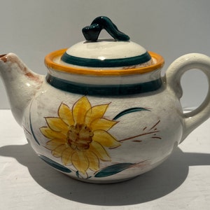 May include: White ceramic teapot with a green and orange striped lid and a painted sunflower design.