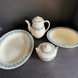 May include: A set of four white ceramic pieces with blue floral designs. The set includes a teapot, a sugar bowl, and two oval serving dishes.