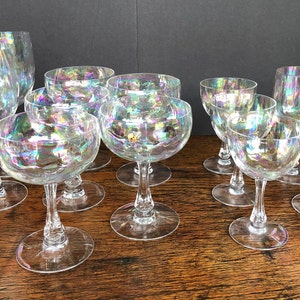 May include: A set of 10 iridescent glass wine glasses. The glasses have a rainbow-like sheen and are arranged on a wooden surface.