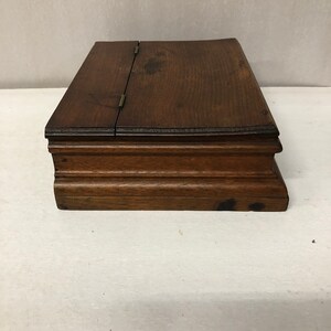 May include: A dark brown wooden box with a hinged lid and a decorative molding around the edge.