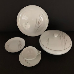 May include: A set of white porcelain dishes with a delicate floral design. The set includes a large platter, a covered serving dish, a small plate, a cup, and a saucer.