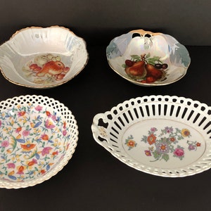 May include: Four decorative porcelain bowls with floral and fruit designs. The bowls are white with gold accents and feature intricate details. Two of the bowls have a lattice design around the rim.