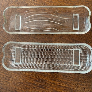 May include: Two clear glass serving dishes with a corn on the cob design. The top dish has a smooth surface with lines that resemble corn husks. The bottom dish has a textured surface that resembles the kernels of corn.