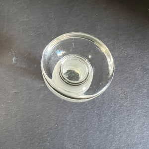 May include: A clear glass bottle stopper with a wide, flat top and a smaller, round opening in the center.
