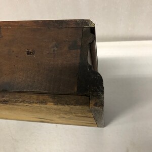 May include: Close-up of the bottom edge of a wooden drawer with a dark brown finish. The drawer has a simple design with a slightly rounded edge.