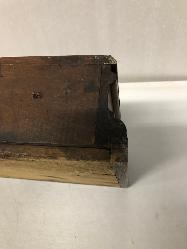 May include: Close-up of the bottom edge of a wooden drawer with a dark brown finish. The drawer has a simple design with a slightly rounded edge.