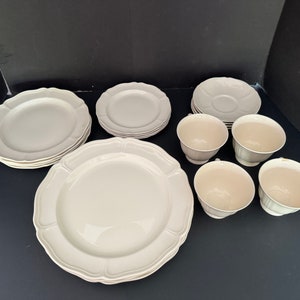 May include: A set of white porcelain dinnerware with a scalloped edge. The set includes a large dinner plate, a smaller salad plate, a saucer, and four teacups.