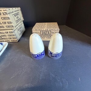 Peut inclure: Deux sali&egrave;res et poivri&egrave;res en c&eacute;ramique blanche avec des bandes &agrave; motifs bleus. Les sali&egrave;res et poivri&egrave;res sont &agrave; c&ocirc;t&eacute; d'une bo&icirc;te qui indique "Churchill of England Salt & Pepper". Les bo&icirc;tes sont blanches avec du texte noir.