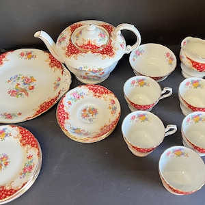 May include: A vintage tea set with a red and gold floral pattern. The set includes a teapot, creamer, sugar bowl, and six teacups and saucers.