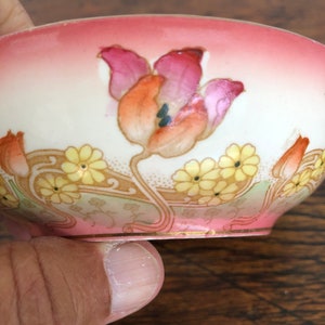 May include: A small, white porcelain bowl with a pink rim and a floral design. The bowl features a large pink and orange tulip with yellow flowers and green leaves.
